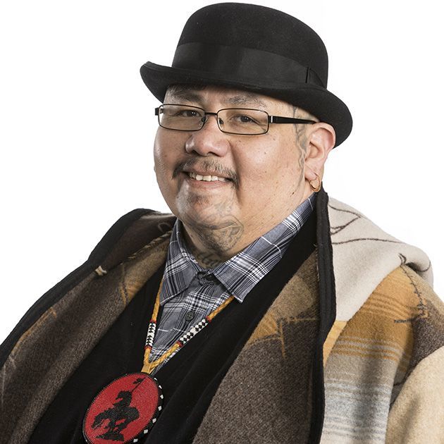A man smiling wearing a checkered collard shirt and a top hat with a white background.