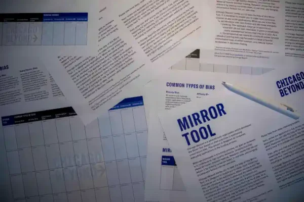 Scattered sheets of paper featuring charts and text, one titled Mirror Tool. A pen rests on the papers. The documents discuss Common Types of Bias and are from Chicago Beyond.