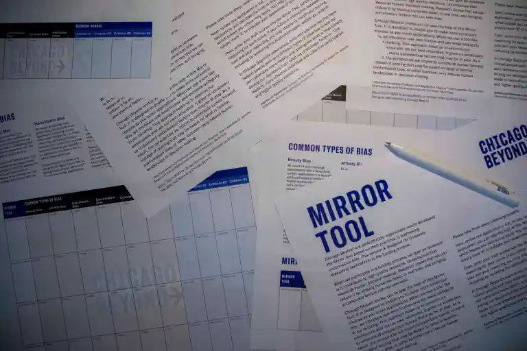 Scattered sheets of paper featuring charts and text, one titled Mirror Tool. A pen rests on the papers. The documents discuss Common Types of Bias and are from Chicago Beyond.