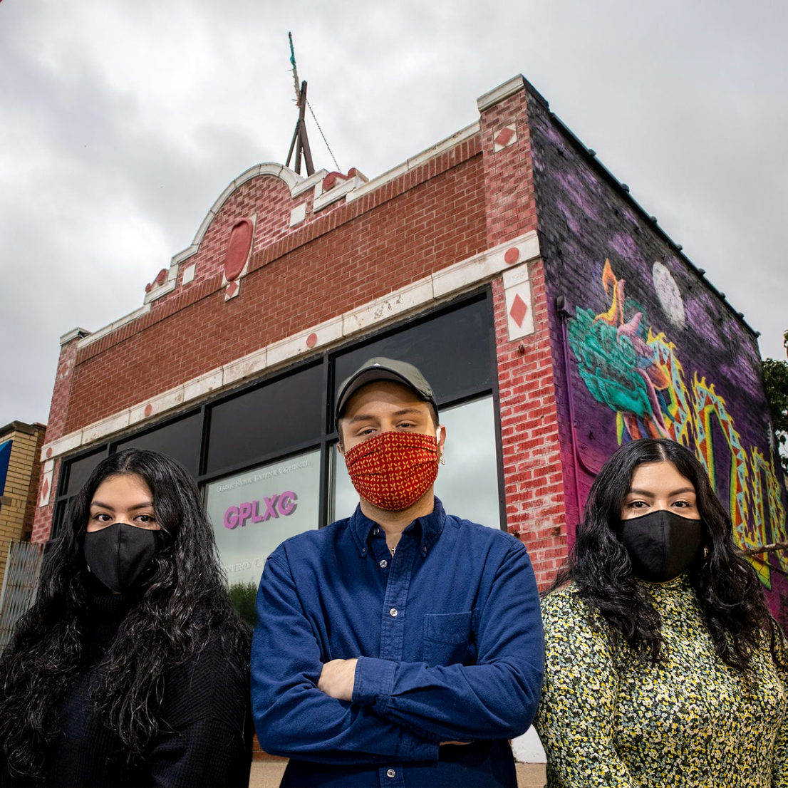 Three people wearing face masks, standing in front of a red brick building with the letters GPLXC on the window.